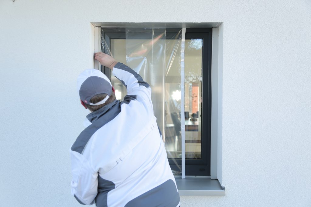 Klauss-Klebeband-003 Ein Maler klebt mit Folie von Klauss-Klebeband ein kleines Fenster ab