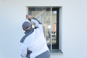 Ein Maler klebt mit Folie von Klauss-Klebeband ein kleines Fenster ab