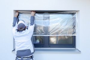 Ein Maler klebt mit Folie von Klauss-Klebeband ein Fenster ab