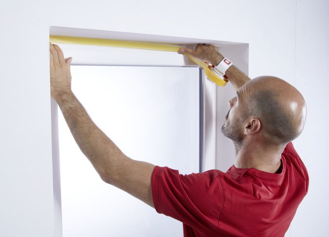 Ein Maler klebt mit der ProTaper Edition von Klauss-Klebeband einen Fensterrahmen ab